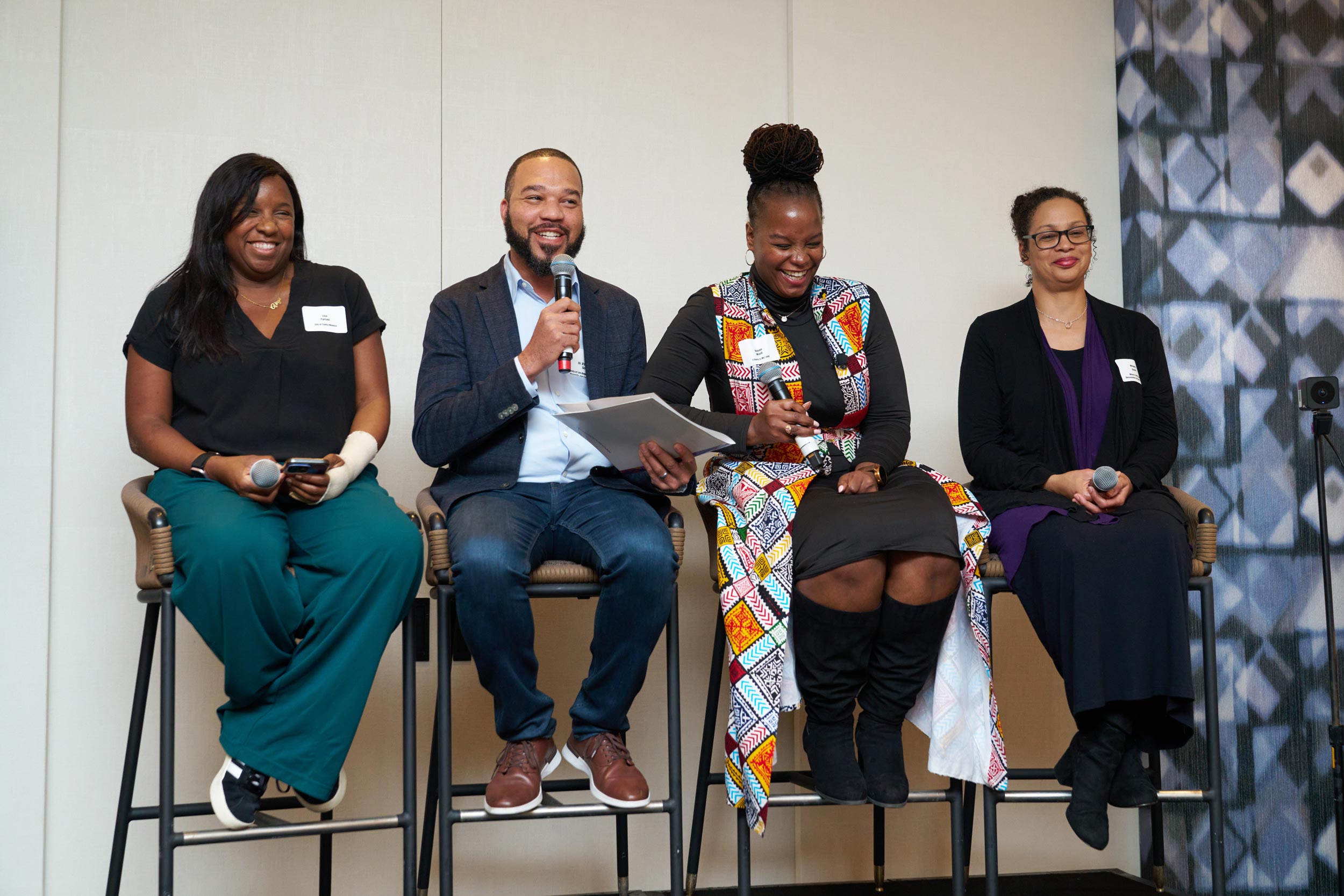 Group of four people sitting in high stools speaking into a microphone gather in Santa Monica for the first in-person convening in our Restoration Through Reparations series.