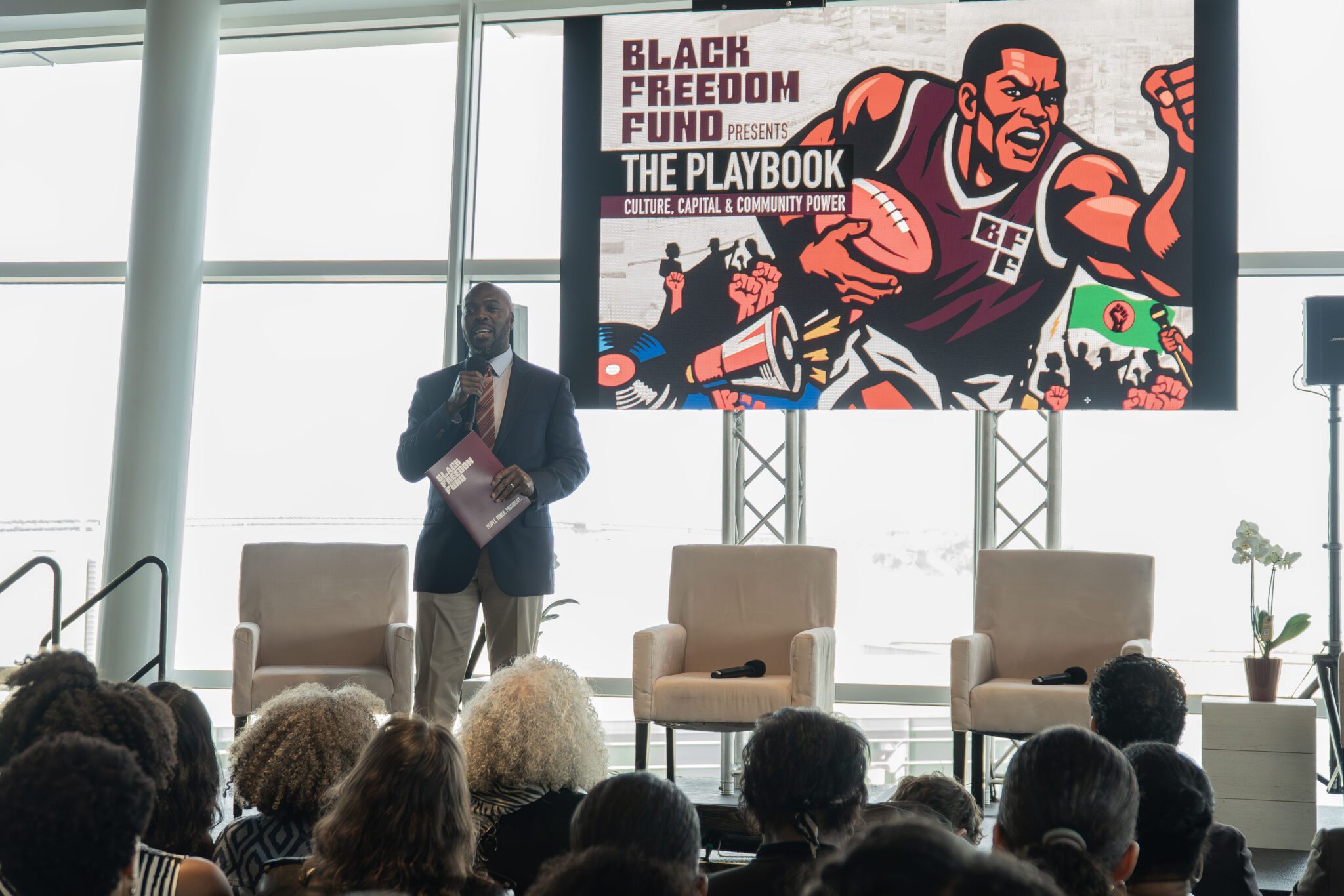 BFF CEO Marc Philpart holding a microphone in front of a seated crowd with display behind him that reads The Playbook