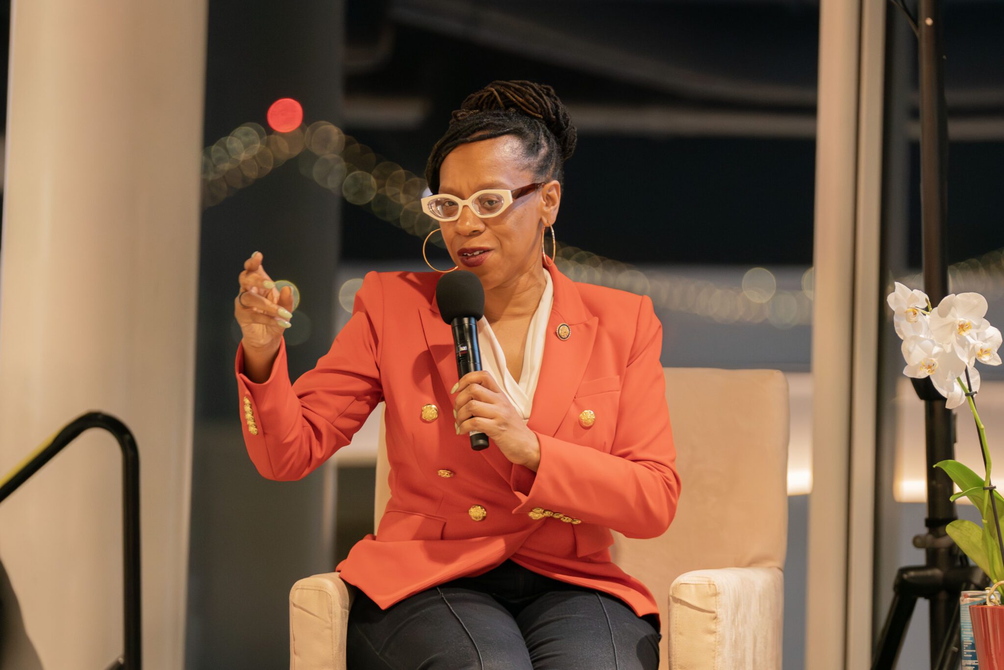 Congresswoman Lateefah Simon seated holding a microphone and speaking to a crowd