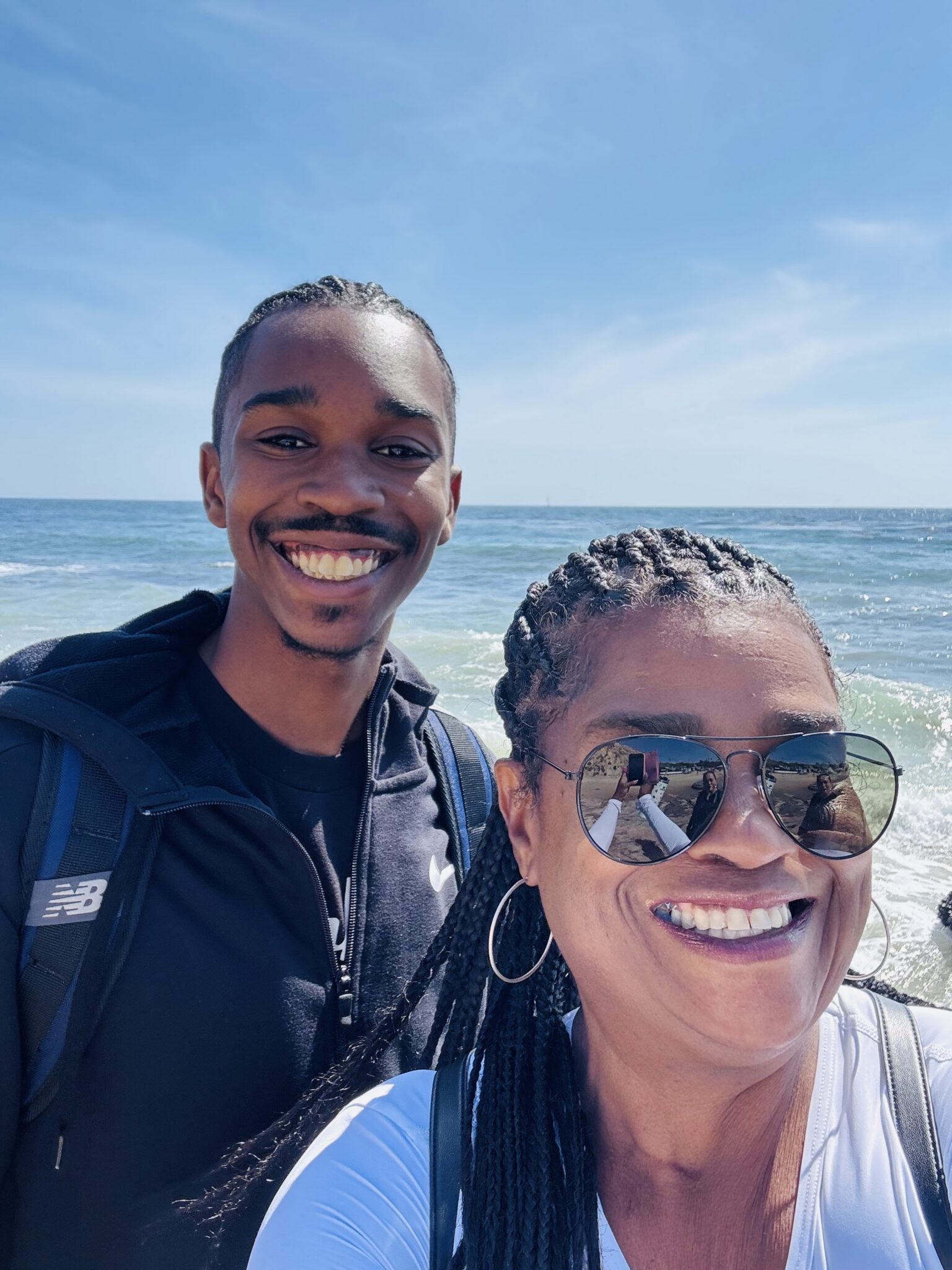 picture of young man and woman taking a selfie at the beach, in front of the ocean.